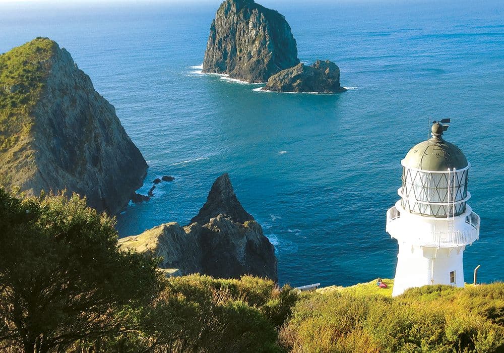 Cape Brett Lighthouse on the headland with Piercy Island and the Hole in the Rock visible offshore.